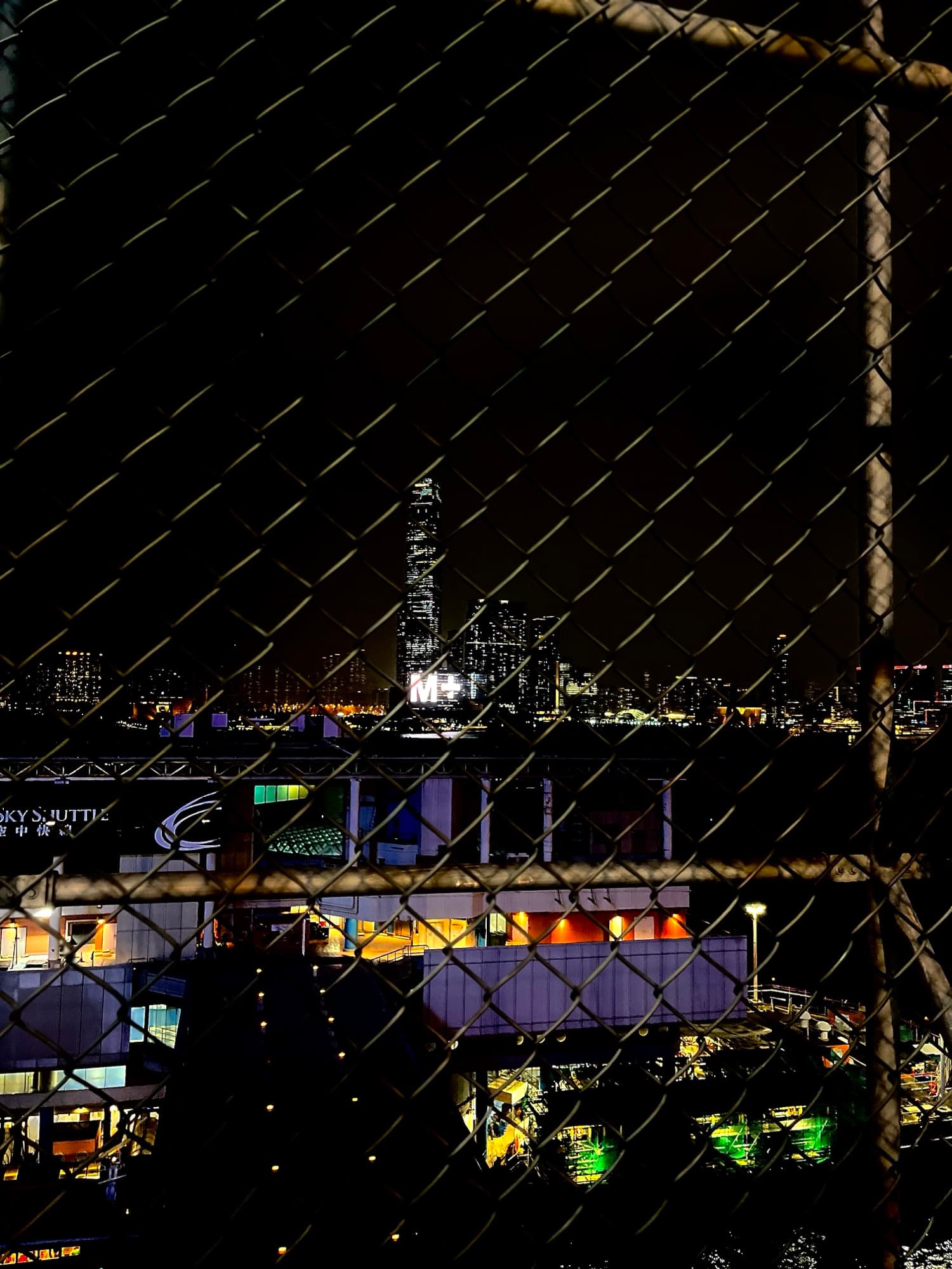夜晚從球場鐵網望出去,香港維港一帶夜景同綠草足球場